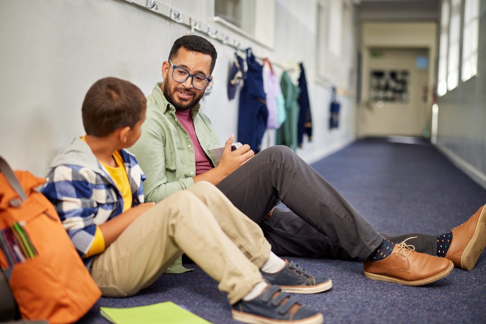 Male teacher sitting in a hallway with a student